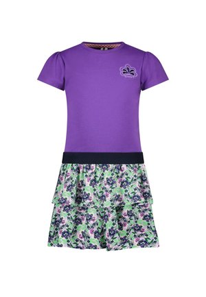 Haut violet à manches courtes avec petit logo fleur et jupe fleurie à couches superposées en vert, violet et blanc, reliés par une ceinture noire.