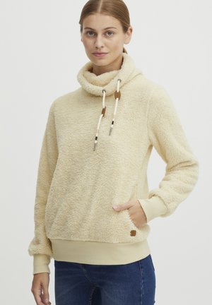 Pull-over en polaire à col montant en crème. Il présente une finition douce et texturée, une poche avant et des cordons de serrage avec des accents en bois.