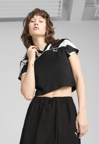 Juodas trumpas sportinis viršus su trumpomis rankovėmis, su baltais akcentais ir logotipu. Suderintas su laisvais juodais šortais su elastine juosta.