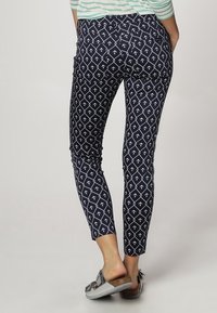 Námořnické kalhoty se vzorem bílých kotviček, úzký střih, střední pas a délka po kotníky, doplněné šedými plážovými sandály.