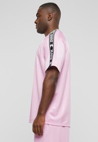 Pink short-sleeve t-shirt with side black and white detailed stripe. Smooth fabric, relaxed fit, crew neckline. Model shown from the side.