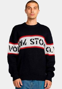 Suéter negro de punto con rayas horizontales rojas y blancas que presenta el texto "VOLCOM STONE CO." Cuello barco, mangas largas, corte relajado.