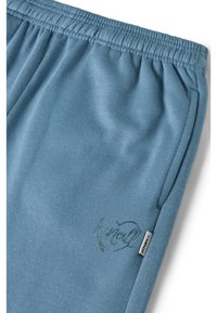Lichtblauwe katoenen joggingbroek met elastische tailleband, zijzakken en groen geborduurd hartpatroon; met merklabel op de zijnaad.