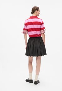 Rødt og rosa stripete polo-skjorte med korte ermer, kombinert med et svart plissert skjørt. Har en ribbestrikket krage og elastisk livlinje.