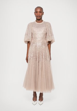 Robe en tulle pailleté de couleur beige clair, avec des manches bouffantes, une taille cintrée et une jupe fluide. Une paire de talons blancs complète le look.