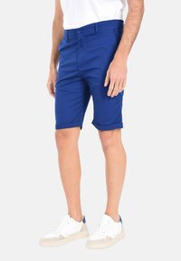 Pantaloni corti blu in cotone con vestibilità slim, dotati di chiusura a bottoni e orli arrotolati, abbinati a sneaker bianche.