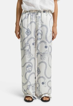 Pantalon blanc ample avec des motifs nautiques bleu, comprenant des cordages, des ancres et des médaillons. Tissu doux avec une taille élastique.