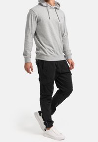 Grå hættetrøje med snører, parret med sorte cargo bukser med flere lommer og hvide sneakers. Casual, afslappet pasform.