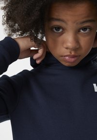 Sudadera azul marino con un cuello alto, con una textura suave y un logo blanco en el pecho. El diseño es casual y ajustado.