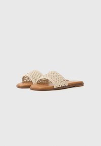Sandali scivolati beige intrecciati con una fascia spessa e suola piatta marrone. Presentano un design aperto e un materiale naturale testurizzato.