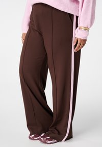 Bruine brede broek met een zachte textuur, met roze zijstrepen. Gecombineerd met kastanjebruine sportschoenen.