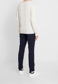 Haut beige clair à manches longues en matériau doux, associé à un pantalon bleu marine et des baskets blanches. Design simple et coupe décontractée.