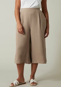 Beige wijde culottes van gestructureerde stof, met een hoge taille en zijzakken. Gepaard met witte slip-on sandalen.