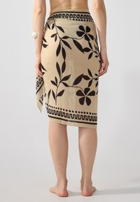 Beige wrap skirt with black floral pattern, featuring a wavy border. Lightweight fabric and a secure tie closure at the waist.