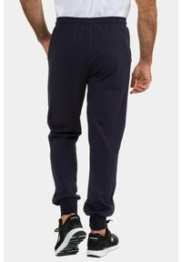 Marineblaue Jogginghose mit elastischem Bund und Bündchen, mit einer glatten Textur. Kombiniert mit schwarzen Sportschuhen, die eine lockere Passform zeigen.