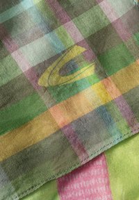 Geverfde sjaal in een zachte, lichte stof. Kenmerkt zich door kleurrijke groene, roze en blauwe vierkanten met een semi-transparante textuur en een subtiel logo.