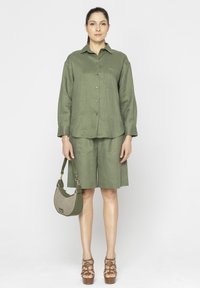 Oliwkowa lniana koszula z guzikami w połączeniu z dopasowanymi szortami. Dodatki to strukturalna zielona torebka oraz brązowe sandały na platformie.