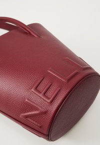 Red leather bucket bag with textured surface and embossed lettering. Features rounded base and two sturdy handles for carrying.