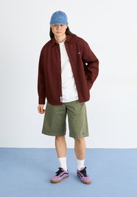 burgundy button-up shirt, white T-shirt, olive green shorts, purple sneakers, denim cap; casual and layered outfit with contrasting colors.