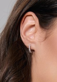 Srebrna kolczyk w formie obręczy z rzędem lśniących, przezroczystych kamieni szlachetnych, zaprojektowany w zakrzywionym kształcie, noszony w przekutym uchu.