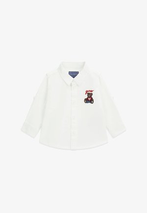 Camisa blanca de manga larga con cuello abotonado, que presenta un oso bordado y el texto "guess" en el lado izquierdo del pecho. Tejido de algodón suave.