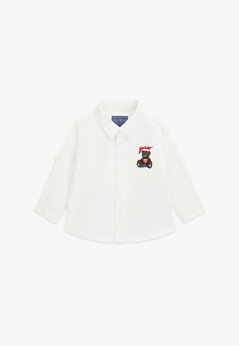 Camicia bianca a maniche lunghe con colletto button-down, caratterizzata da un orso ricamato e testo "guess" sul petto sinistro. Tessuto di cotone liscio.