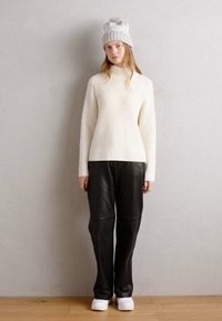 Pull à col roulé blanc à côtes associé à un pantalon en cuir noir et des baskets blanches à plateforme ; le mannequin porte un bonnet en tricot gris.