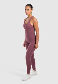 Bordeaux sportieve jumpsuit met een aansluitend ontwerp, ronde halslijn, brede bandjes en een naadloze textuur, gecombineerd met witte schoenen.