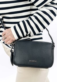 Person trägt schwarzen und weißen gestreiften Pullover und hält eine schwarze Ledertasche mit Textur und silbernem "EMILY & NOAH"-Logo.