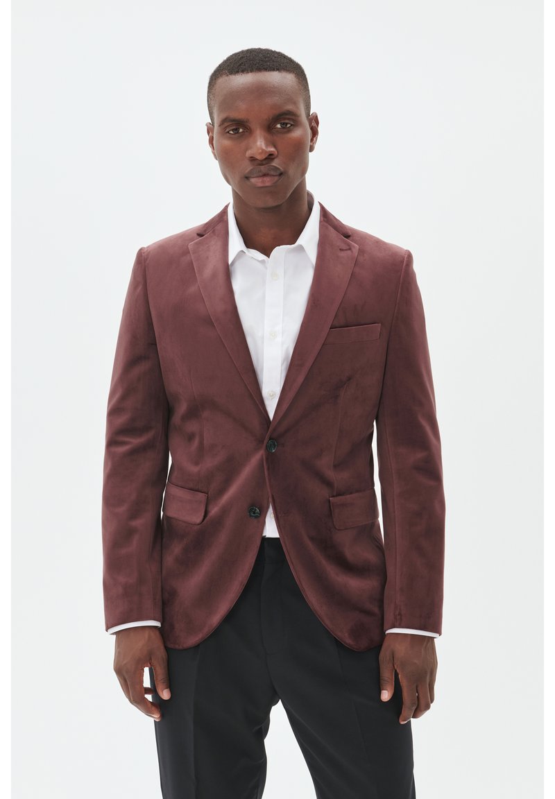 Burgunder-velours Blazer mit Reverskragen, zwei Fronttaschen und einfacher Knopfverschluss, kombiniert mit einem weißen Hemd und schwarzen Hosen.