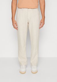 Beige linnebyxor med rak passform, med flat front, bälteshällor och en lätt textur. Kombineras med vita sneakers.