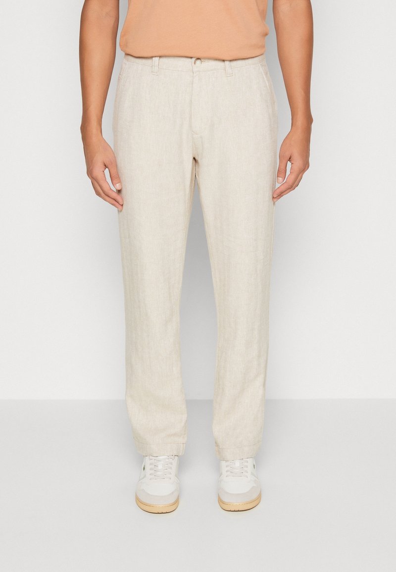 Beige linnebyxor med rak passform, med flat front, bälteshällor och en lätt textur. Kombineras med vita sneakers.