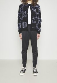 Svart kavaj med ett geometriskt mönster i blått, tillsammans med svarta joggers med vita sidosträck och svarta skor.