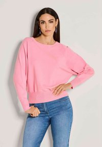 Rosa Strickpullover mit langen Ärmeln und Rundhalsausschnitt, ausgestattet mit einem taillierten Bund. Kombiniert mit blauen Skinny-Jeans. Glatte Textur.