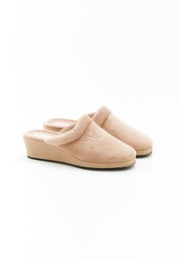 Chaussons en fausse fourrure beige avec une semelle compensée, un bout arrondi et des détails de coutures décoratives sur le dessus. Matériau texturé et design confortable.