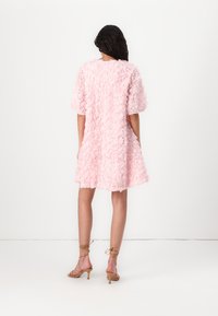 Roze jurk met een 3D-rozenstructuur, korte mouwen en een uitlopende silhouette, gecombineerd met lichtbruine strap sandalen.