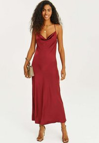 Burgundské saténové maxi šaty s volným dekoltom, tenkými ramienkami a hladkou textúrou. Skombinované s malou šedou kabelkou a sandálmi na opätku.