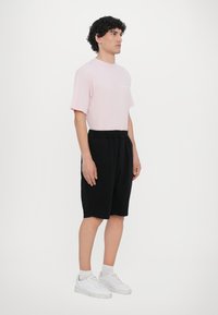 Light pink cotton t-shirt paired with black cotton shorts. Model wears white sneakers and white socks. Simple, relaxed-fit design.