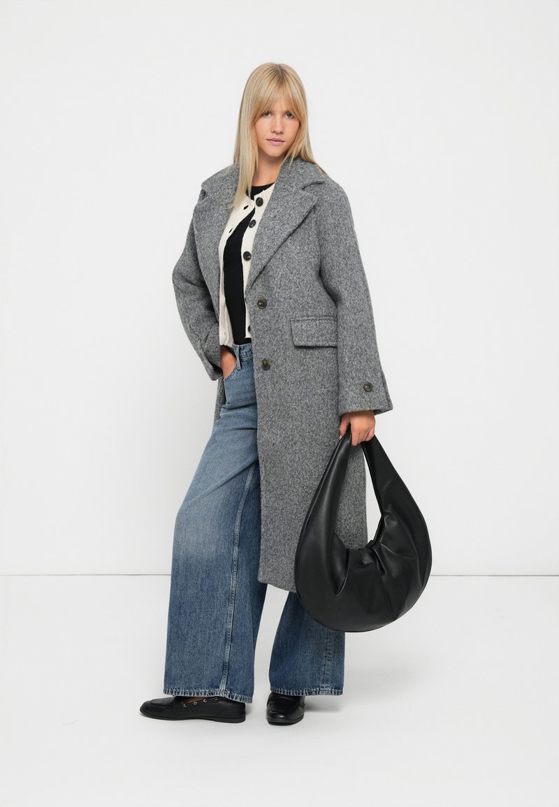 Manteau en laine gris avec de grands revers, fermeture à boutons, associé à un pull noir, un jean large en denim et un sac hobo noir.