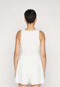 Valge ilma varrukateta jumpsuit, millel on istuv keha ja laiad lühikesed püksid. Sile tekstuur lihtsa disainiga, vaadates selja poolt.