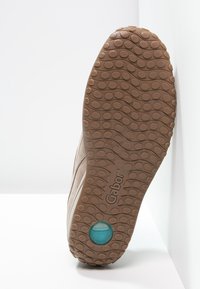 Chaussure beige clair avec une semelle en caoutchouc texturée présentant des motifs circulaires. Elle comporte un accent bleu au talon et des détails de coutures sur la tige.