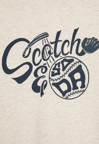 Beige szövet, amelyen egy tengerészkék grafika látható, a "Scotch" szóval és egy baseball dizájnnal, beleértve a varrás részleteit és egy baseball ütőt.