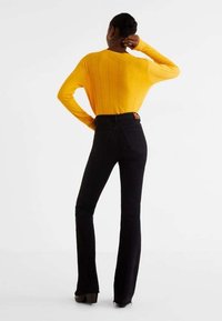 Maglione giallo a maglia, aderente e maniche lunghe, con costine verticali, abbinato a jeans neri in denim a vita alta e svasati. Scarpe con tacco nere.