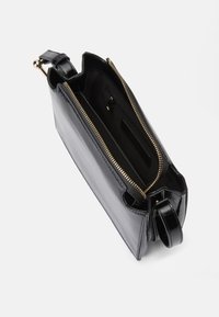 Černá kožená kabelka na zip, s kovovými doplňky ve zlaté barvě. Uvnitř se nachází kapsa na zip a otevřená kapsa pro lepší organizaci.