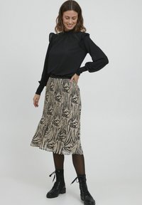 Melnas garām piedurknēm blūze ar frills pleciem, apvienota ar bēšu un melnu rakstotu midi svārku. Modelis valkā melnus auklējamus zābakus.