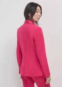 Fitted pink blazer with a notched collar, smooth texture, and single back vent, paired with a matching pant suit.