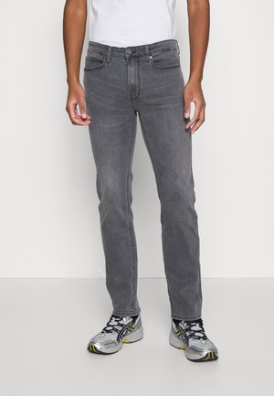 Graue Denim-Jeans mit slim fit, Fünf-Taschen-Design und mittelhoher Taille, kombiniert mit grau-gelben Sportschuhen.