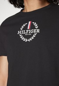 Musta puuvillapaita, jossa valkoinen logo, joka esittää laakerinoksaa ja punavalkoisen sinisen raidallisen yksityiskohdan. Pyöreä kaula-aukko ja lyhyet hihat.