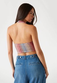 Halter neck crop top in multicolor textured fabric with a wavy pattern, paired with high-waisted blue denim jeans featuring back pockets.