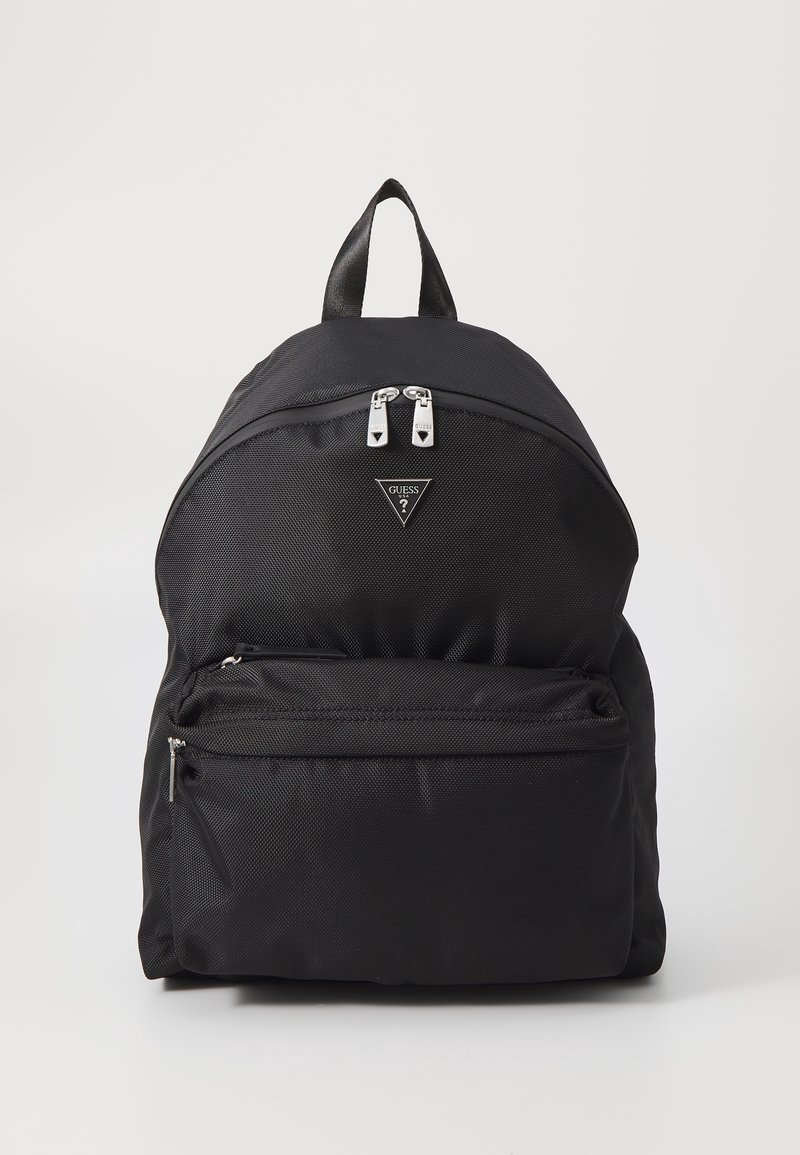 Sac à dos noir Guess avec poche zippée frontale, double fermeture éclair supérieure et une poignée de transport unique sur un fond clair uni.